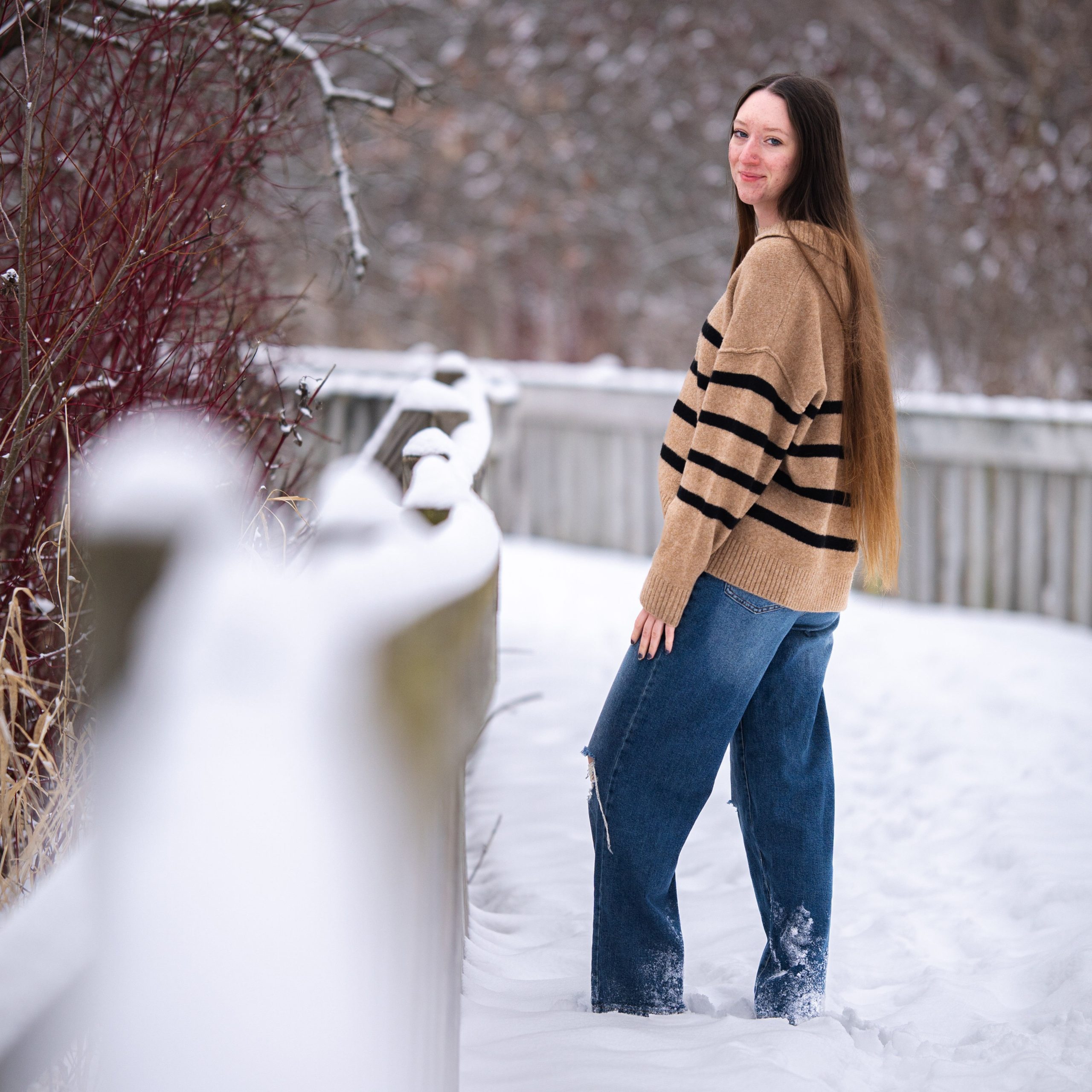 Lady with long hair sanding on a snow covered walkway with red plants on the left side